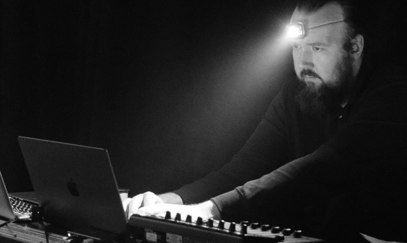 James Bull, in front of a mixing desk and laptop, wearing a pair of headphones